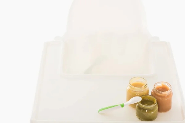 Vue grand angle de trois bocaux avec purée d'enfant et cuillère sur chaise haute isolé sur fond blanc — Photo de stock