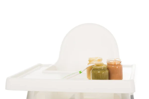 Primo piano vista di tre vasi con purea di bambino e cucchiaio su seggiolone isolato su sfondo bianco — Foto stock