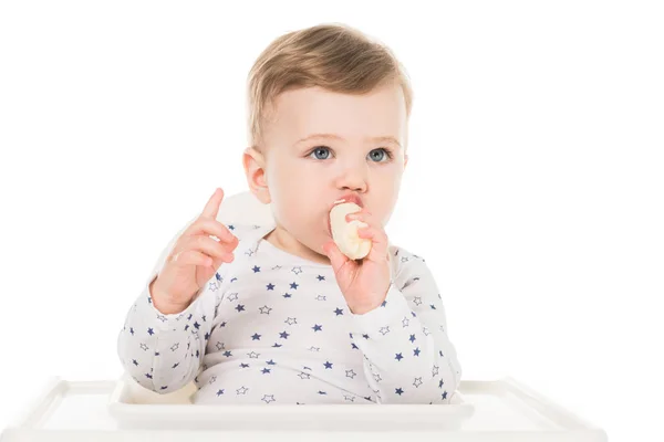 Хлопчик з піднятим пальцем їсть банан ізольовано на білому тлі — стокове фото