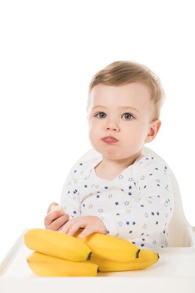 Comer bebê menino sentado em cadeira alta com bananas isoladas no fundo branco — Fotografia de Stock