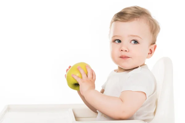 Baby boy eating apple and sitting in highchair isolated on white background — Stock Photo