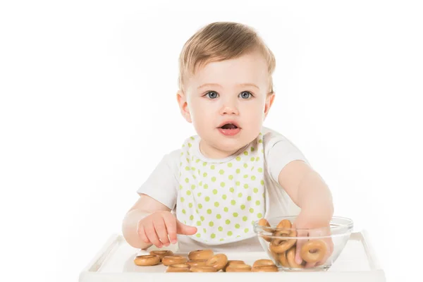 Niño sonriente comiendo rosquillas y sentado en trona aislado sobre fondo blanco - foto de stock