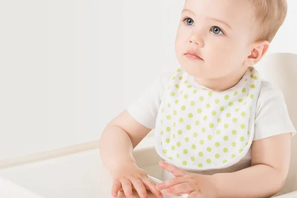 Porträt eines kleinen Jungen in Latz, der im Hochstuhl auf weißem Hintergrund sitzt — Stockfoto