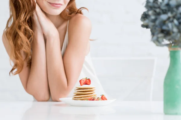 Tiro recortado de mujer joven tomando panqueques con fresa para el desayuno en casa - foto de stock