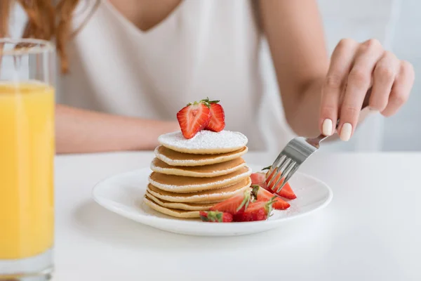 Tiro recortado de la mujer que tiene panqueques con fresa para el desayuno - foto de stock