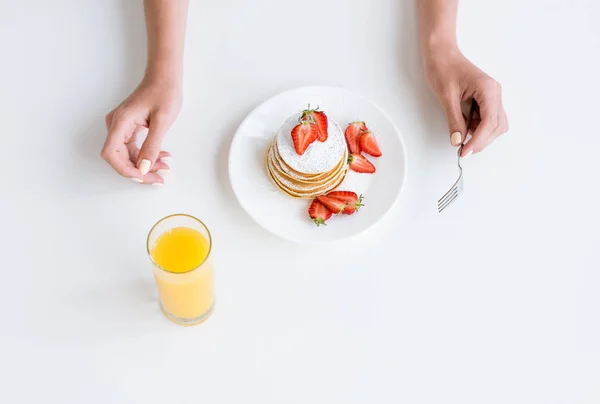 Tiro recortado de mujer tomando jugo de naranja y panqueques con fresa para el desayuno - foto de stock