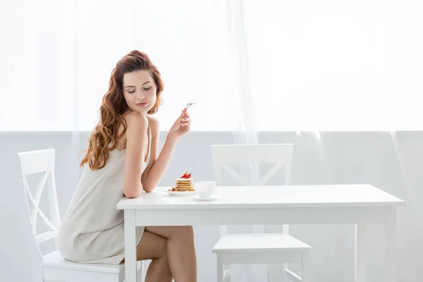 Sinnliche junge Frau sitzt zu Hause am Tisch mit Erdbeer-Pfannkuchen — Stockfoto