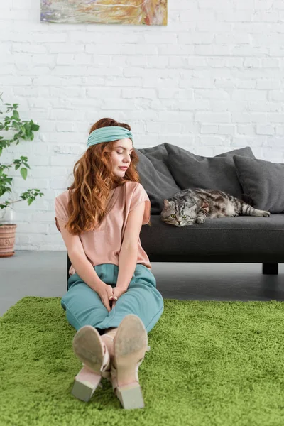 Belle jeune femme assise sur le sol près de son chat tabby à la maison — Photo de stock