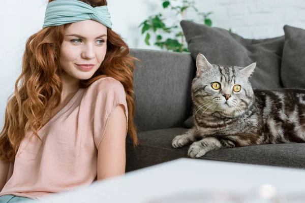 Hermosa joven sentada cerca adorable tabby gato en casa - foto de stock