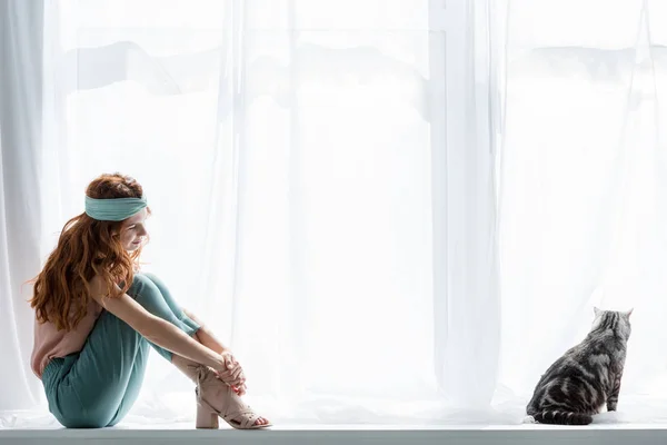 Attractive young woman sitting on windowsill with cute tabby cat — Stock Photo