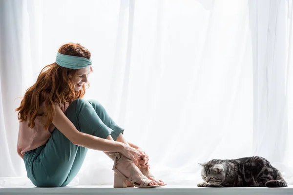 Attrayant jeune femme assise sur le rebord de la fenêtre avec chat tabby — Photo de stock