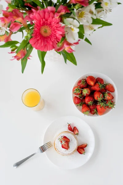 Vista superior de sabrosos panqueques con fresas y flores en jarrón - foto de stock