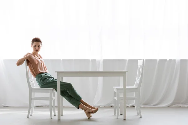 Vista lateral de la joven solitaria sentada en la mesa en casa - foto de stock