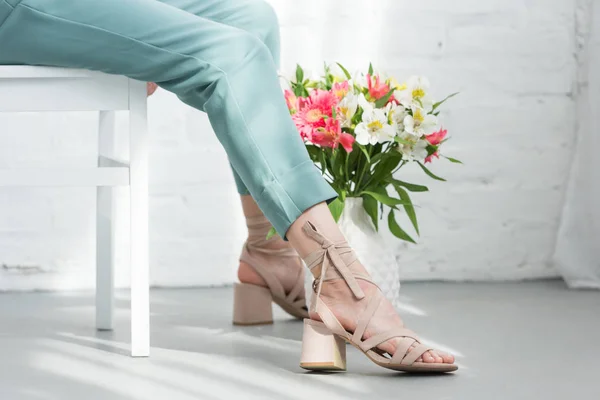 Cropped shot of woman sitting on chair with flowers on floor in front of white brick wall — Stock Photo