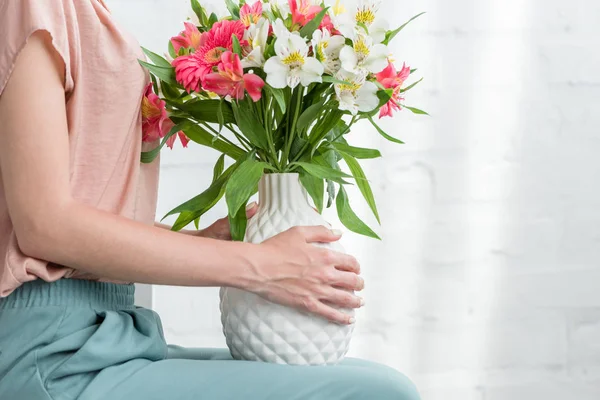 Tiro recortado de mujer con flores en jarrón delante de la pared de ladrillo blanco - foto de stock