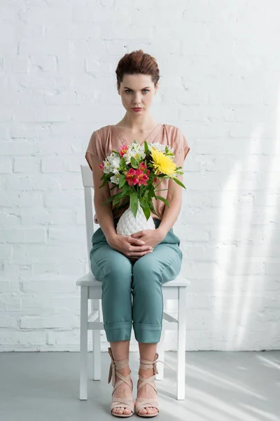 Beautiful young woman with flowers in vase in front of white brick wall — Stock Photo