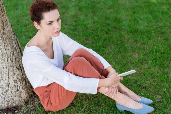 Schöne junge Frau mit Smartphone sitzt auf Gras im Park — Stockfoto