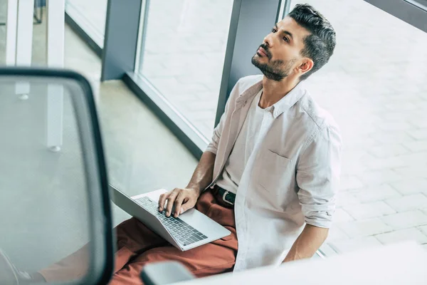 Vista ad alto angolo di uomo d'affari premuroso in abiti casual seduto sul pavimento con computer portatile e guardando in alto — Foto stock