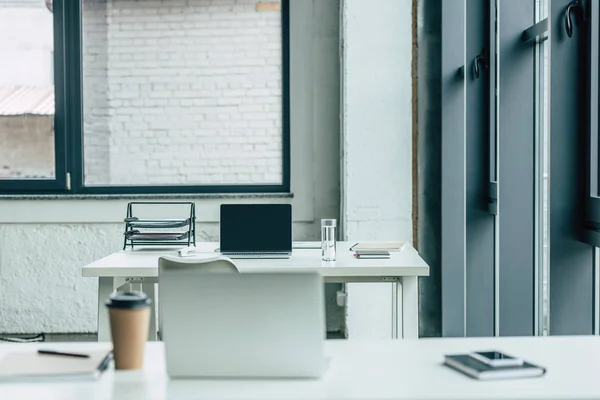 Mesas de escritório com laptops, café para ir e vidro de água, cadernos e bandeja de documentos — Fotografia de Stock