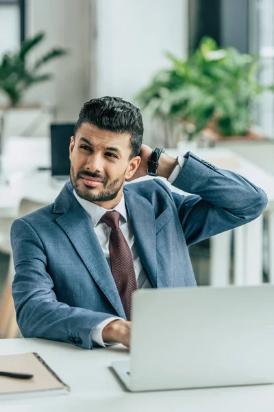 Nachdenklicher Geschäftsmann, der am Arbeitsplatz sitzt, wegschaut und die Hand hinter dem Kopf hält — Stockfoto