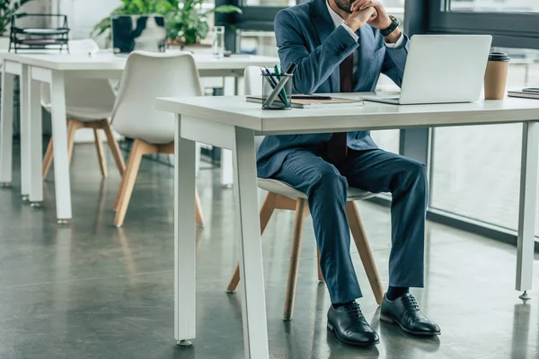Обрезанный вид бизнесмена в костюме сидящего на рабочем месте в офисе — стоковое фото