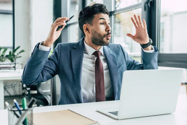 Aufgeregter Geschäftsmann schaut weg und zeigt Wow-Geste, während er am Arbeitsplatz in der Nähe von Laptop sitzt — Stockfoto