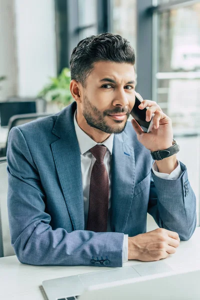 Skeptische Unternehmen blicken beim Telefonieren auf das Smartphone in die Kamera — Stockfoto