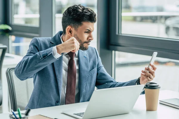 Agresivo hombre de negocios mostrando puño mientras tiene chat de vídeo en el teléfono inteligente - foto de stock