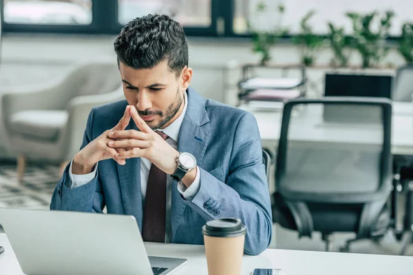 Thoughtful businessman looking at laptop while sitting at workplace — Stock Photo