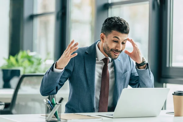 Sorprendido empresario gesto y tocando la cabeza mientras se sienta en el lugar de trabajo - foto de stock