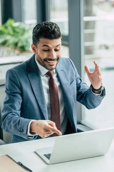 Empresário surpreso mostrando com o dedo no laptop enquanto sentado no local de trabalho — Fotografia de Stock