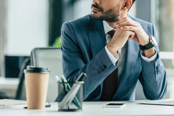 Vista recortada de hombre de negocios sentado en el lugar de trabajo con las manos dobladas — Stock Photo