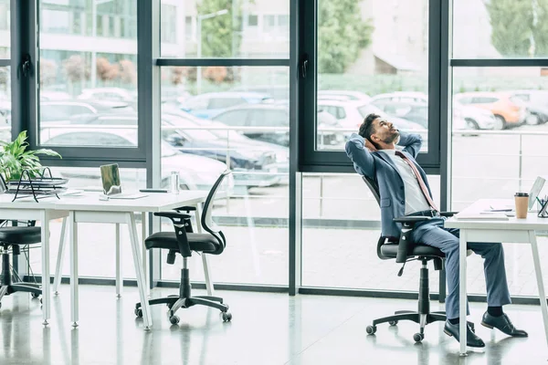 Jeune homme d'affaires se reposant tout en étant assis sur le lieu de travail dans un bureau spacieux moderne — Photo de stock