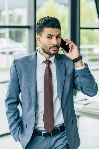 Молодий впевнений бізнесмен розмовляє по смартфону, тримаючи руку в кишені — стокове фото