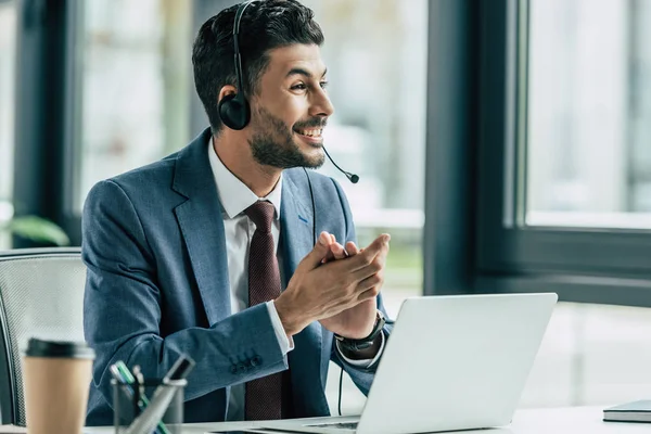 Cheerful call center operator looking away while sitting at workplace — Stock Photo