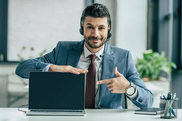 Fröhlicher Callcenter-Betreiber zeigt mit dem Finger auf Laptop mit leerem Bildschirm — Stockfoto