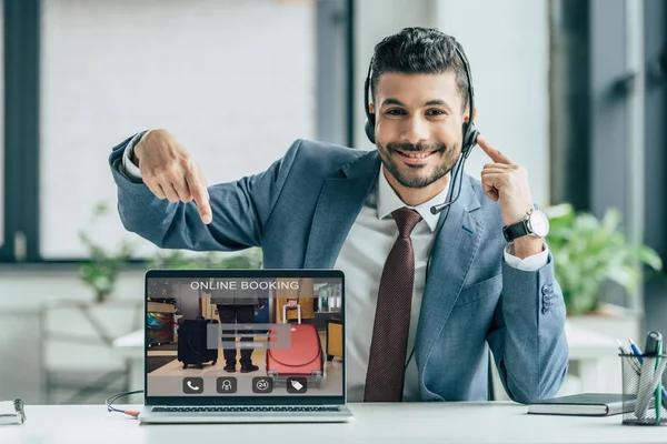 Cheerful call center operator pointing with finger at laptop with online booking website on screen — Stock Photo