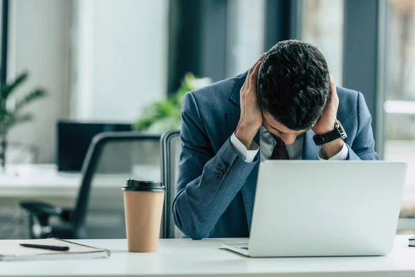 Uomo d'affari esausto seduto sul posto di lavoro vicino al computer portatile e tazza usa e getta — Foto stock