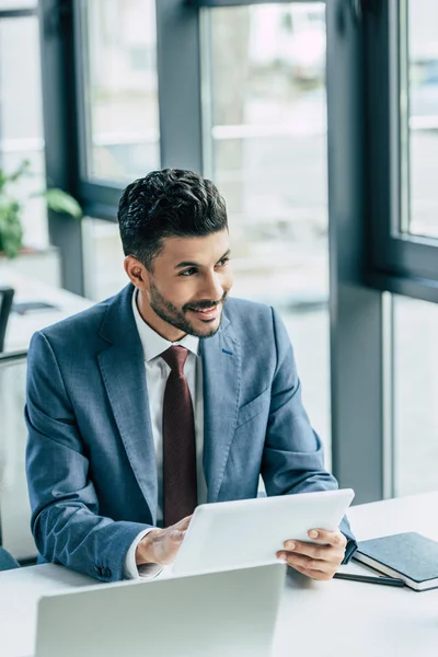 Sonriente hombre de negocios mirando hacia otro lado mientras sostiene la tableta digital - foto de stock