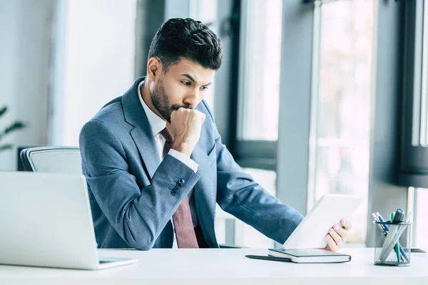Pensativo hombre de negocios mirando tableta digital mientras está sentado en el lugar de trabajo - foto de stock