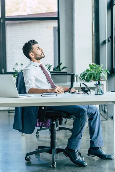 Operatore premuroso call center guardando altrove mentre seduto sul posto di lavoro vicino laptop e auricolare — Foto stock