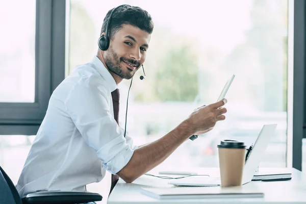 Fröhlicher Callcenter-Betreiber hält digitales Tablet in der Hand und blickt in die Kamera — Stockfoto