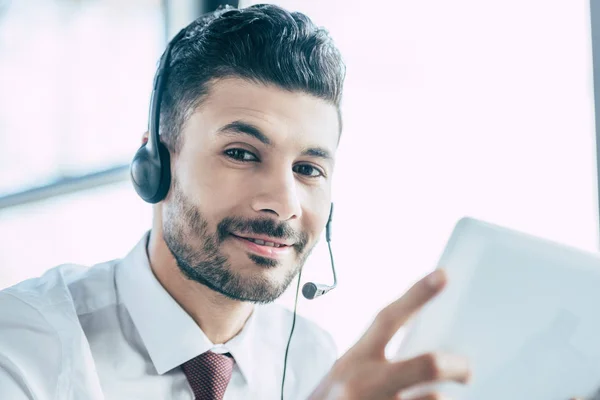 Fröhlicher Callcenter-Betreiber lächelt in die Kamera, während er ein digitales Tablet in der Hand hält — Stockfoto