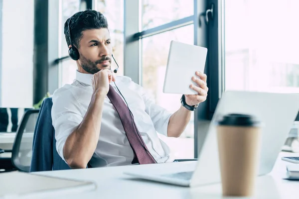 Selective focus of thoughtful call center operator looking away while holding digital tablet — Stock Photo