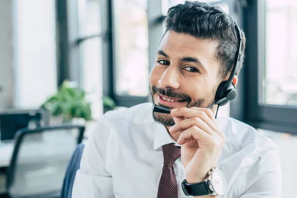 Bello operatore call center sorridente alla fotocamera durante l'utilizzo di cuffie — Foto stock