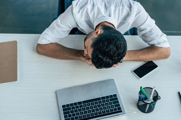 Vista dall'alto di un uomo d'affari esausto che dorme sul posto di lavoro vicino a laptop e smartphone — Foto stock