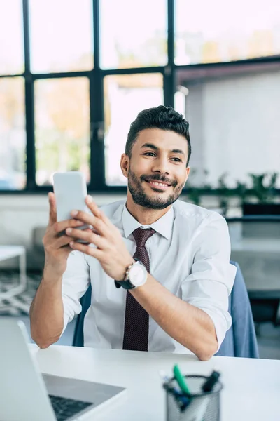 Foco seletivo de empresário alegre olhando embora enquanto segurando smartphone — Fotografia de Stock