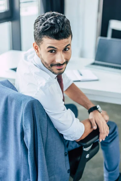 Guapo hombre de negocios sonriendo a la cámara mientras está sentado en el lugar de trabajo - foto de stock