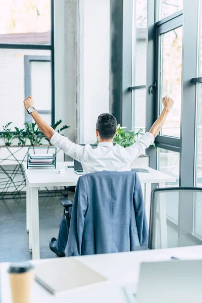 Vista trasera del hombre de negocios cansado estirándose mientras está sentado en el lugar de trabajo - foto de stock