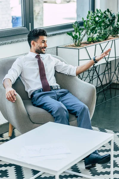 Веселый бизнесмен машет рукой, расслабляясь в кресле — стоковое фото